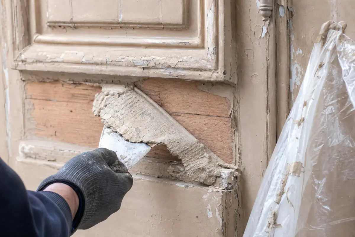 Pâte de décapage bio retirée à la spatule sur une porte cochère, couches anciennes ramollies