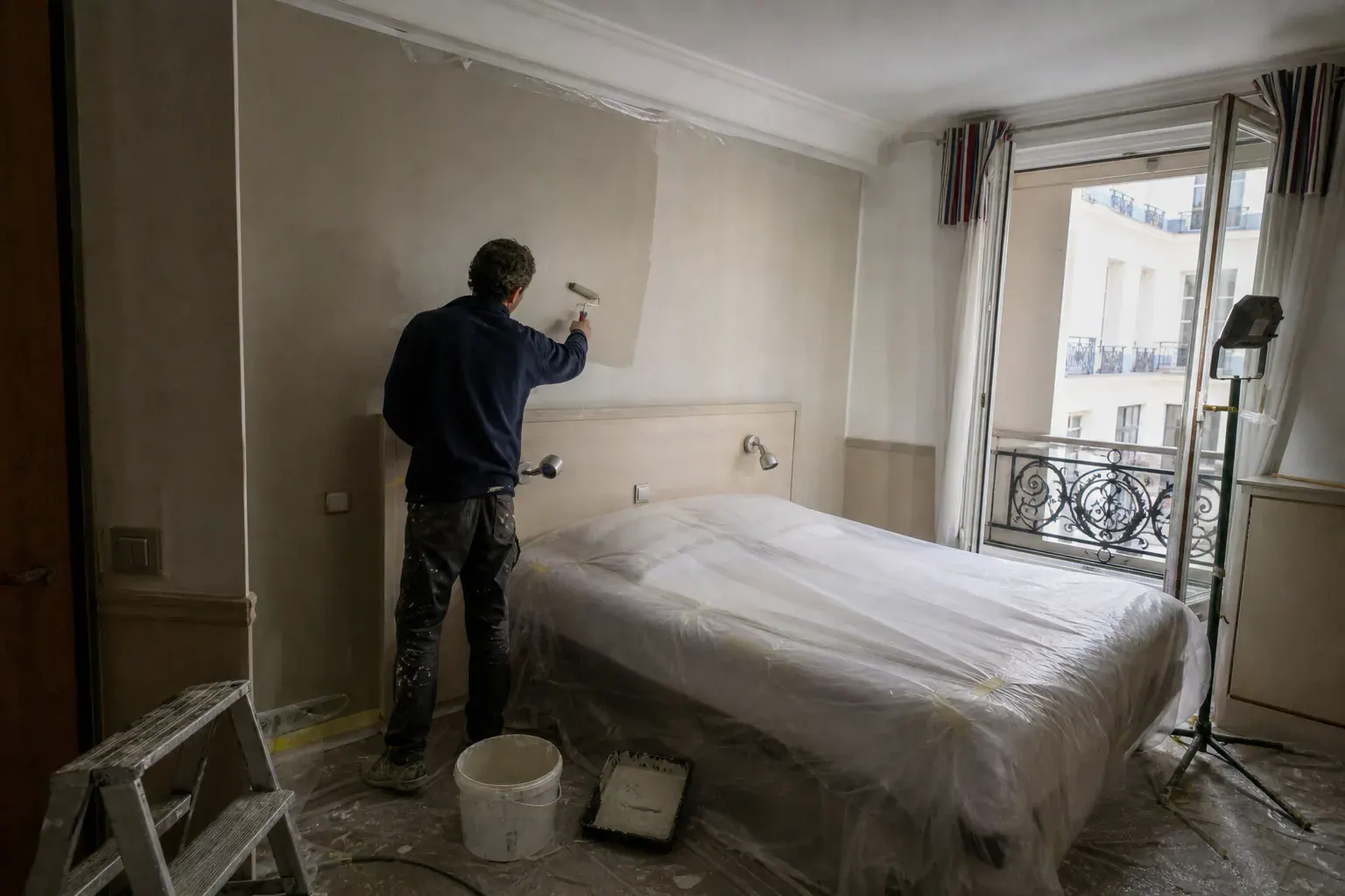 Chambre d’hôtel repeinte entre deux services, lit et mobilier protégés sous bâches