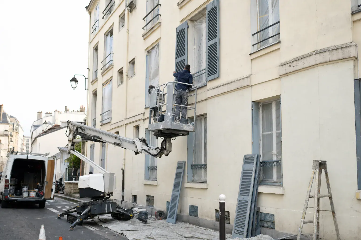 Peintre sur nacelle repeignant les volets battants d’une façade d’immeuble en Île-de-France