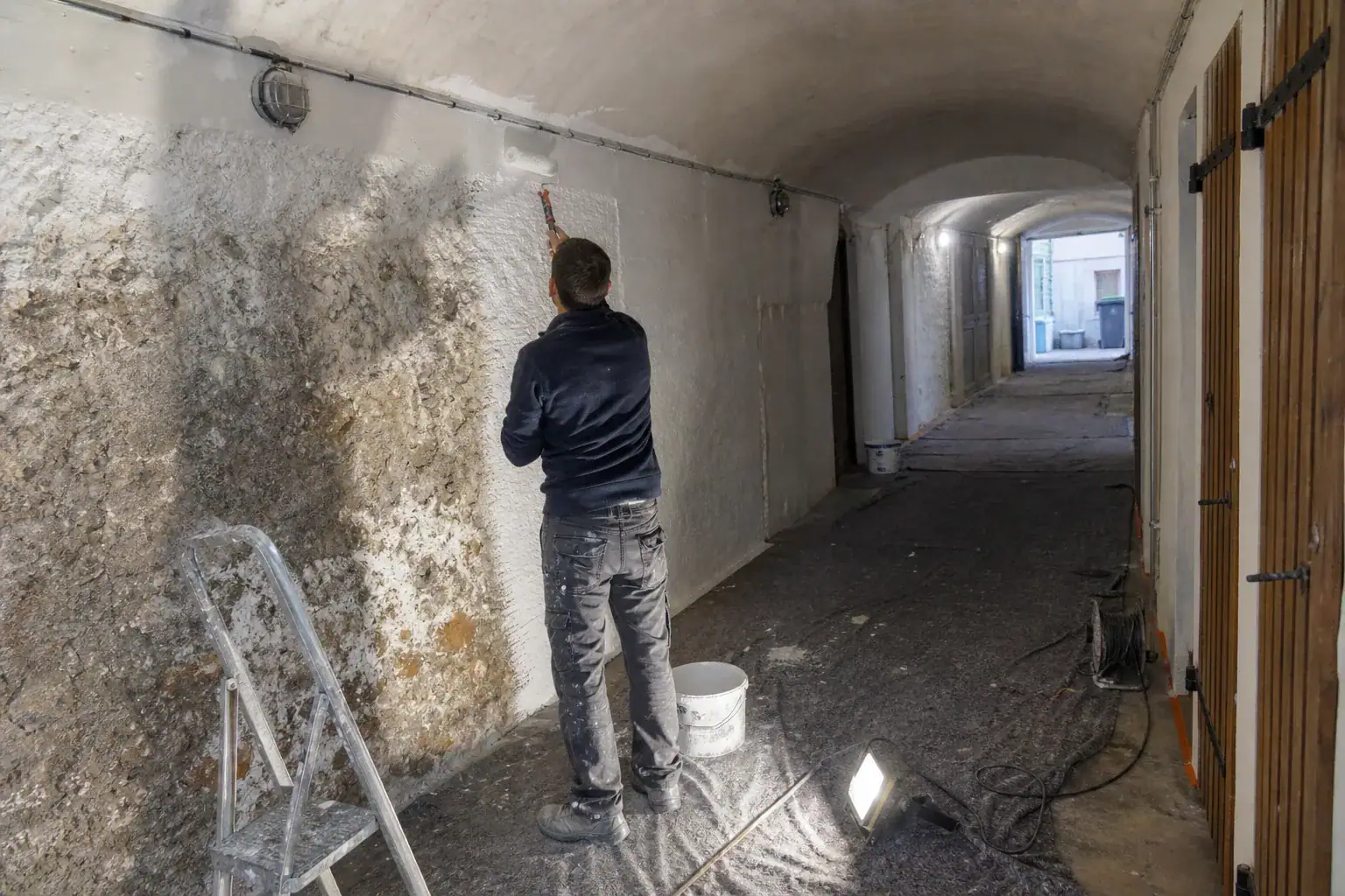 Peinture d’un couloir de caves d’immeuble avec une peinture microporeuse, éclairage de chantier