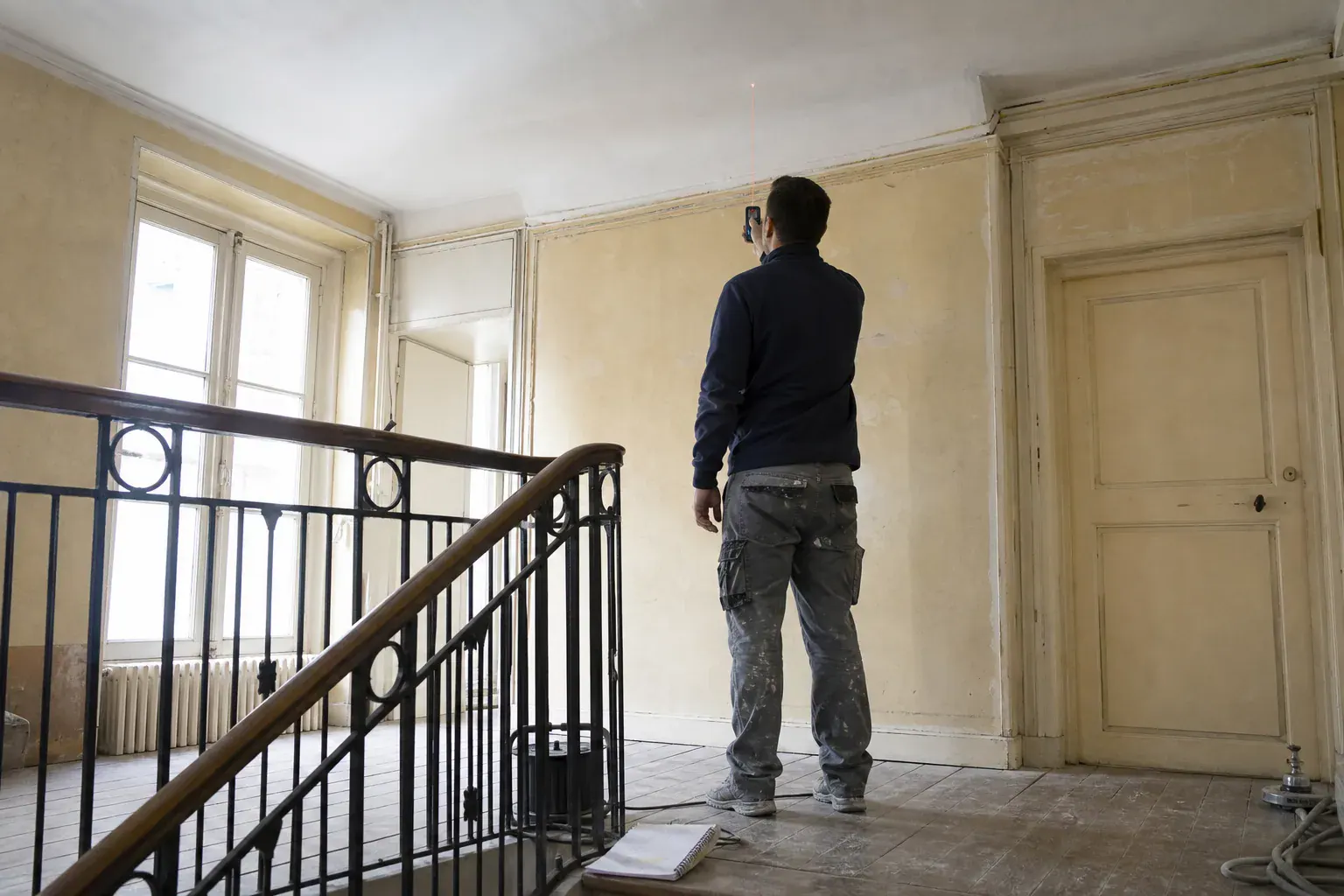 Métré des parties communes d’un immeuble avant chiffrage, mètre laser contre le mur d’un palier
