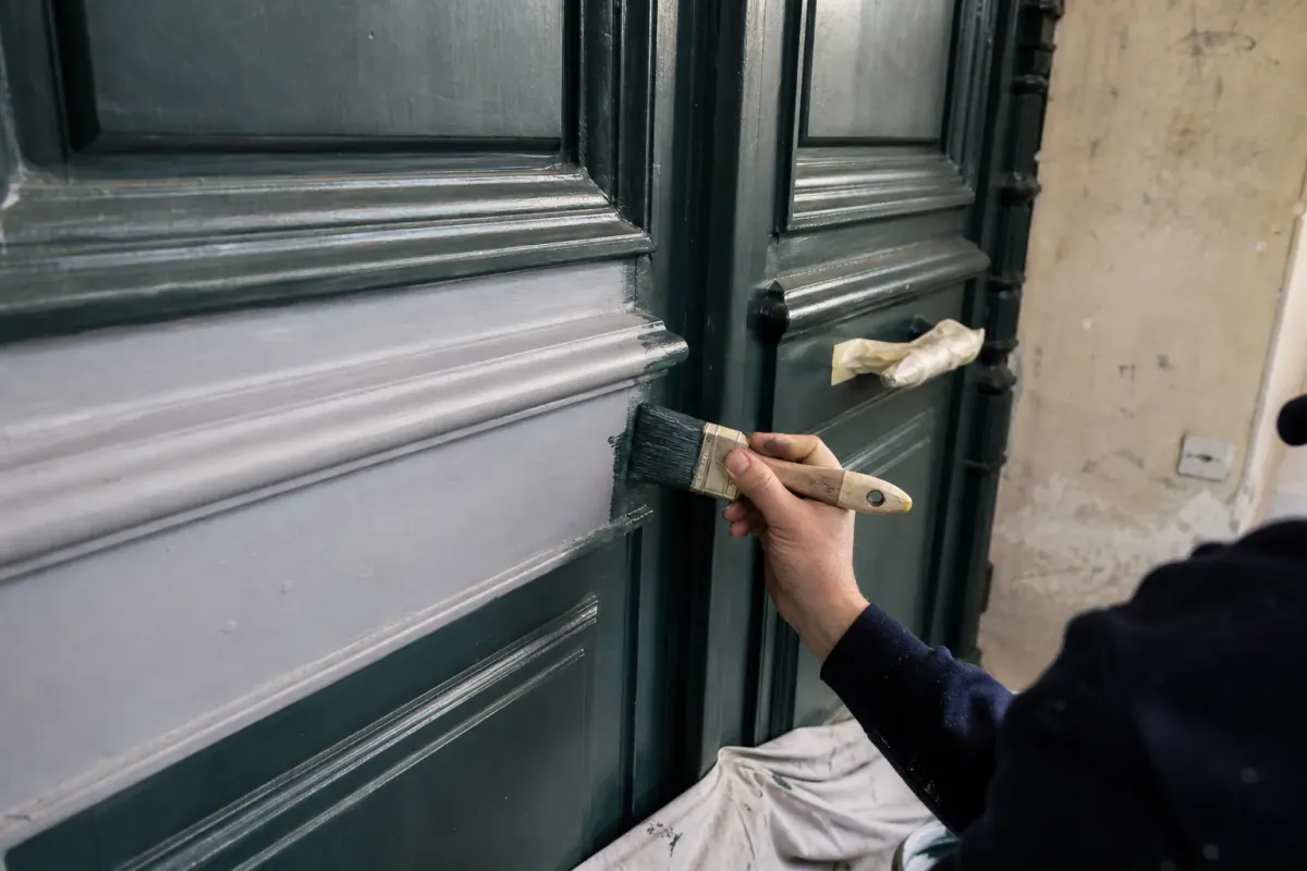 Laquage vantail par vantail d’une porte cochère, couche de laque vert sombre appliquée à la brosse